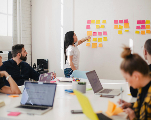 Person sat at laptop, person presenting post-its on a whiteboard